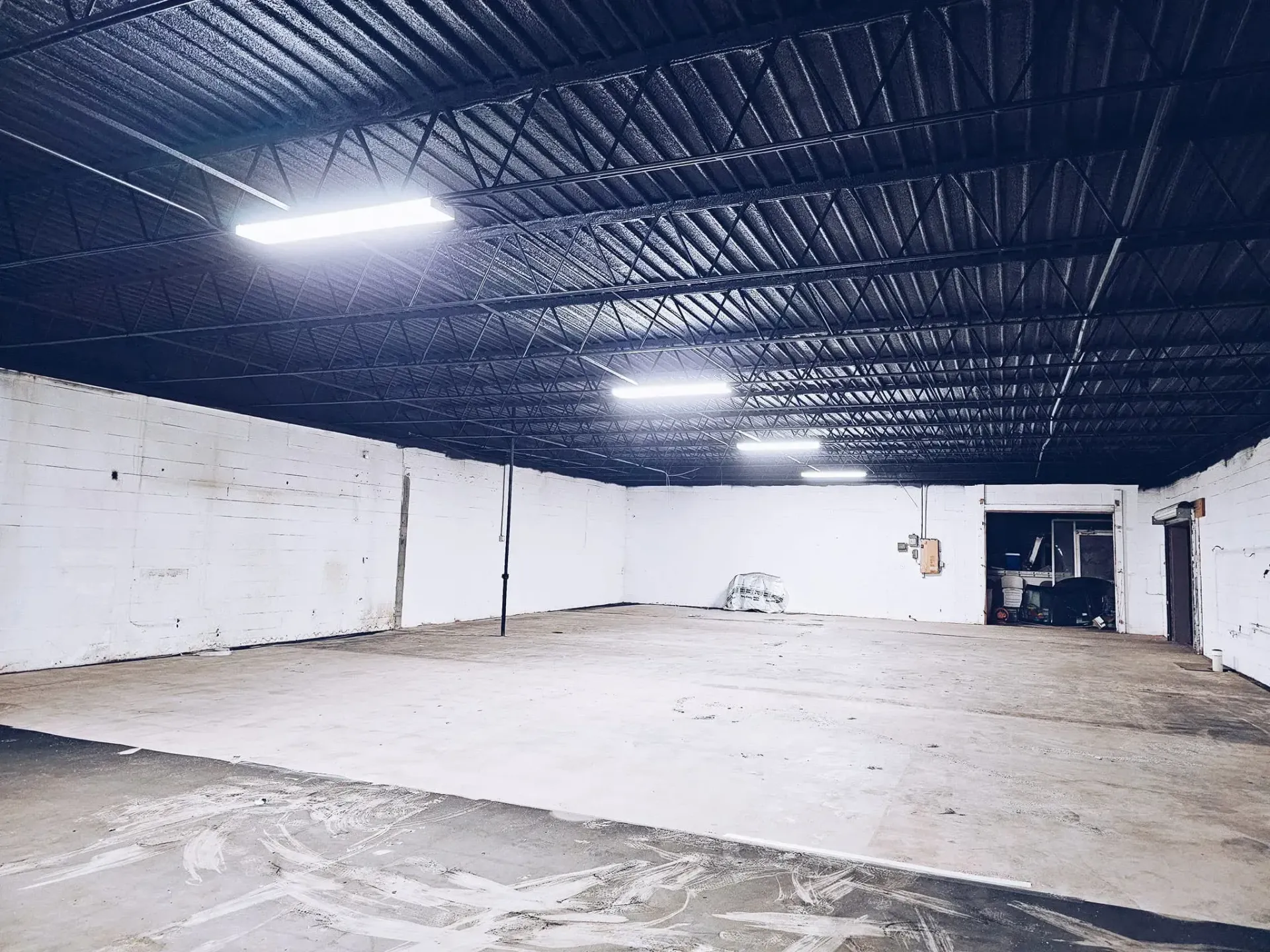 Empty white warehouse with a dark insulated ceiling and fluorescent lights over a concrete floor