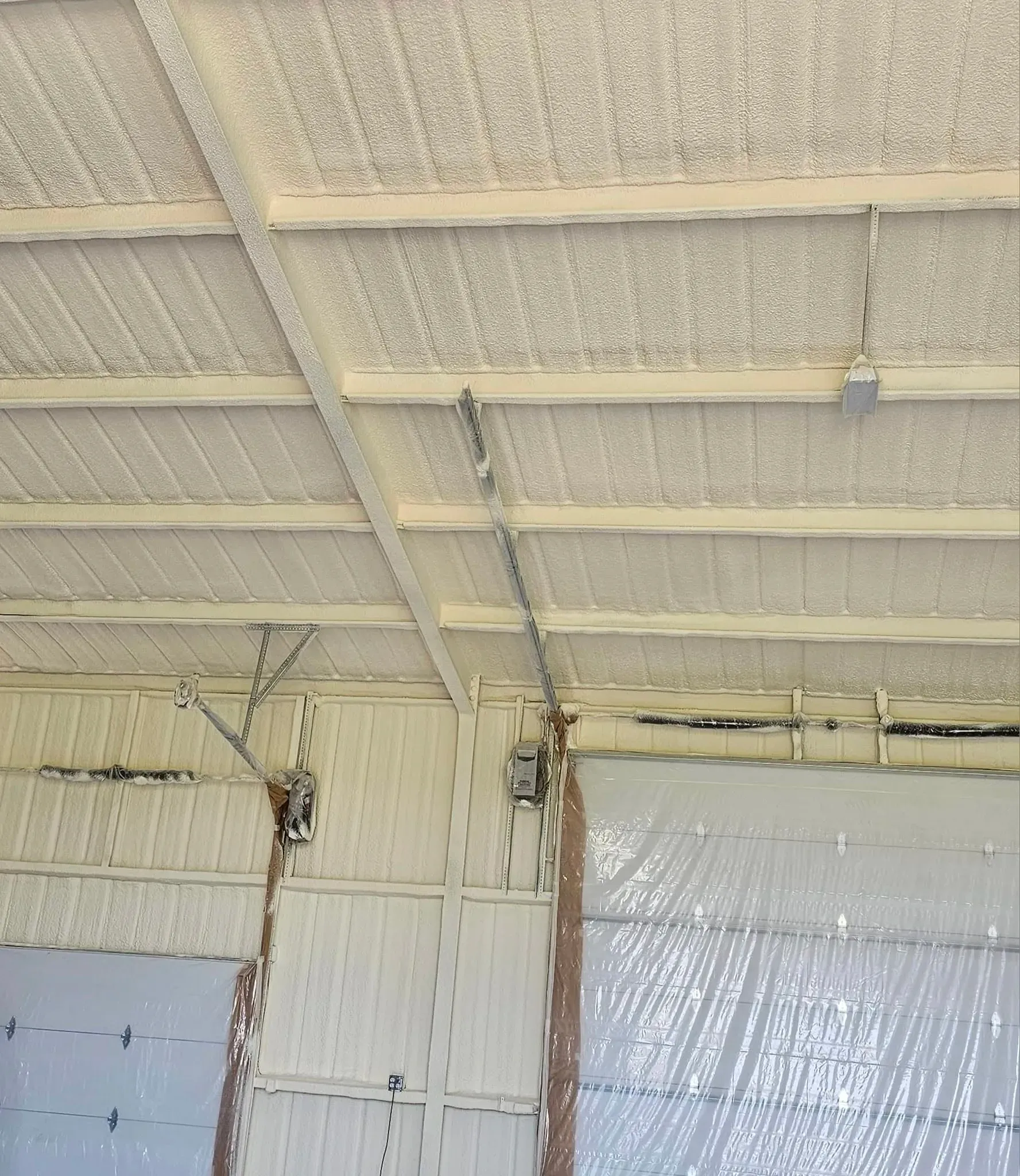 Interior ceiling with spray foam insulation, exposed beams, and hanging wires above a doorway