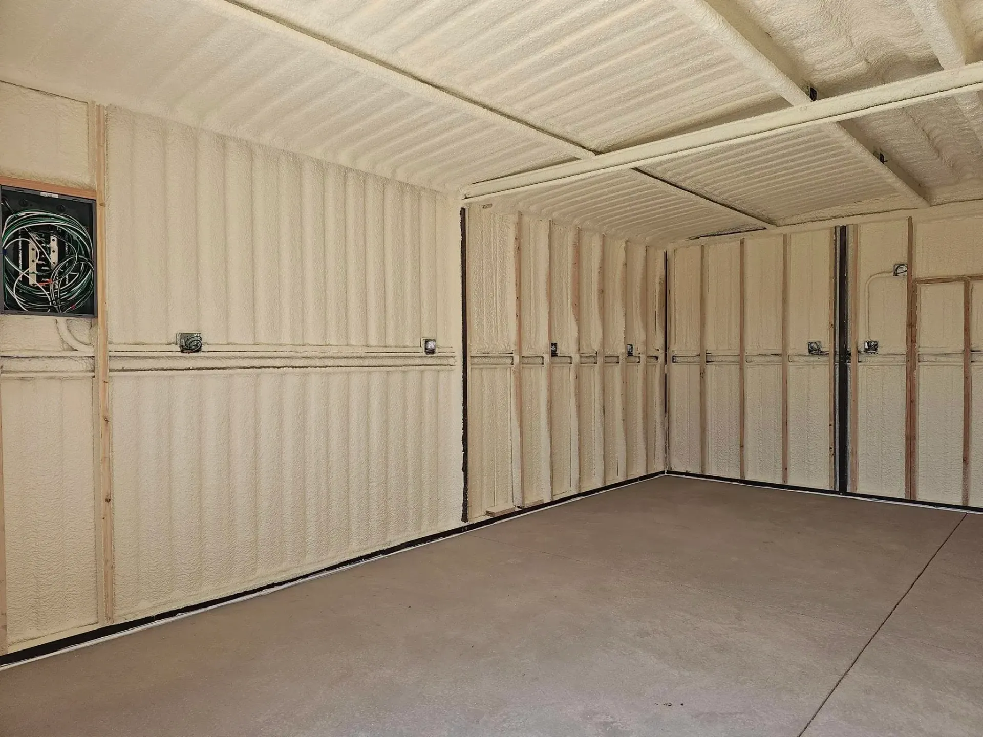 Empty room with spray foam on walls, exposed framing, and a bare concrete floor