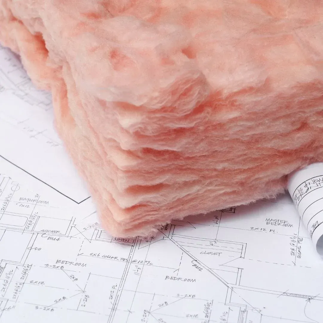 Pink fiberglass insulation batts placed over residential building plans for a Lubbock, TX home