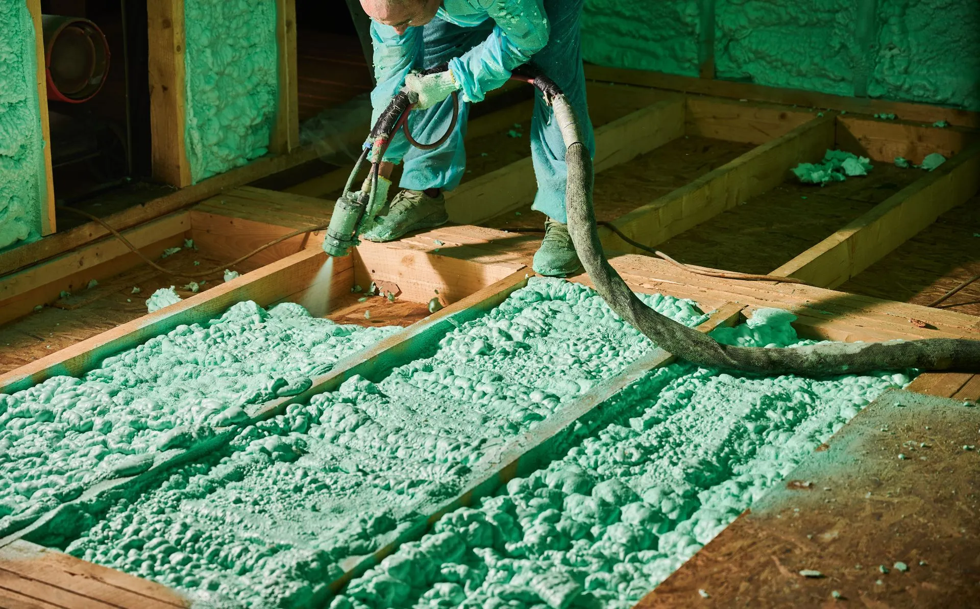A man is spraying green insulation on a wooden floor.